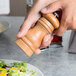 A person using a Fletchers' Mill cherry wooden pepper mill over a plate of salad.