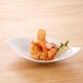 An Arcoroc round porcelain appetizer bowl filled with shrimp on a wooden table.
