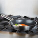 A Vollrath stainless steel non-stick fry pan with vegetables cooking in it on a stove.