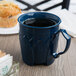 A dark blue Dinex insulated mug with a black drink on a table with muffins.