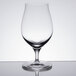A Spiegelau stemmed beer glass with a clear surface on a reflective surface.