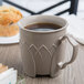 A Dinex Fenwick latte mug filled with coffee sits on a table next to muffins.