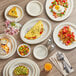 A wood table with Acopa ivory stoneware plates of omelette, fruit salad, and pizza.