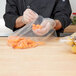 A person in a chef's uniform putting carrots in a plastic food bag.