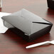 A black Fold-Pak Bio-Pak paper take-out box on a table with a white plastic fork and knife.