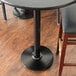 A black Lancaster Table & Seating cast iron table base with two black chairs on a wood floor.
