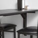 A black table with Lancaster Table & Seating Cantilever Metal Table Brackets under a wall.