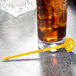 A glass of liquid with ice and a yellow oval stirrer.