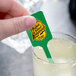 A hand holding a green rectangular plastic stick in a glass of lemonade.