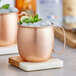A copper Acopa Moscow Mule mug with ice and lime on a marble coaster.
