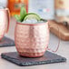 Two Acopa hammered copper Moscow mule mugs on a stone counter with ice and lime wedges.