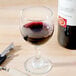 A Libbey wine glass filled with red wine next to a wine bottle.