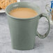 A Cambro Harbor Collection Meadow insulated mug filled with coffee on a saucer with cookies.
