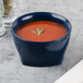 A navy blue Cambro insulated bowl of tomato soup with a sprig of rosemary.