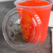 A Fabri-Kal plastic cup with a red drink in it and a clear plastic lid with red and white flavor buttons and a straw slot on a table.