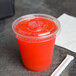 A Fabri-Kal clear plastic lid with a straw slot and flavor buttons on a plastic cup with a red liquid on a grey surface.