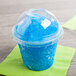 A clear plastic dome lid with a blue straw in a cup of blue slushy.