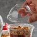 A hand using a Fabri-Kal clear plastic dome lid to cover a cup of granola.