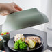 A hand using a Cambro Meadow insulated plastic dome plate cover to protect a plate of food.