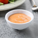 A Tablecraft white round ribbed melamine ramekin filled with tomato sauce on a table.