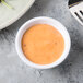 A white Tablecraft ramekin filled with orange sauce on a table.