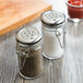 Two Tablecraft glass jars with metal clip-top lids filled with salt and pepper on a table.