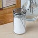 A close-up of a Tablecraft glass jar with a stainless steel clip-top lid filled with white substance.