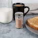 A Tablecraft glass jar of brown powder with a stainless steel clip-top lid on a plate of toast near a glass of milk.