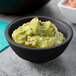 A Tablecraft black round ribbed melamine ramekin filled with guacamole on a table.