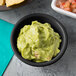 A Tablecraft black round ribbed melamine ramekin filled with guacamole on a table with a bowl of salsa.