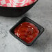 A black Tablecraft melamine ramekin filled with ketchup on a table.