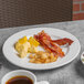 A Libbey Porcelana plate with bacon, eggs, and coffee on a table.