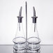 A Tablecraft Siena oil and vinegar cruet set with two glass bottles on a silver stand with metal accents.
