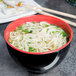 A white melamine bowl of noodle soup with chopsticks and green onions.