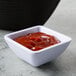 A white Tablecraft square ramekin filled with ketchup on a black surface.