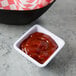 A Tablecraft white square ribbed melamine ramekin filled with ketchup on a table.