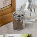 A Tablecraft glass jar with a stainless steel clip-top lid filled with ground black pepper.