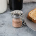 A Tablecraft glass jar of salt with a stainless steel clip-top lid on a plate of toast.
