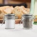 Two Tablecraft glass salt and pepper shakers with stainless steel clip-top lids on a table.