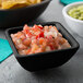 A black Tablecraft ramekin filled with salsa on a table with a bowl of guacamole.