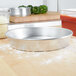 An American Metalcraft heavy weight aluminum pizza pan on a counter with a pizza on top.