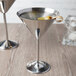 Two stainless steel martini glasses filled with olives on a table in a cocktail bar.