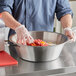A person in gloves stirring food in a Vollrath stainless steel utility bowl.
