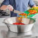 A person cutting vegetables with a knife into a Vollrath stainless steel utility bowl.
