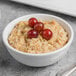 A bowl of oatmeal with raisins and cherries in a white Libbey porcelain bowl.
