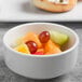 A bowl of fruit in a white Libbey Porcelana bowl with a sandwich on the side.