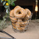 A Clipper Mill chrome plated metal round wire basket holding a bagel with sesame seeds.