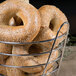A Clipper Mill chrome plated metal wire basket with a bagel topped with sesame seeds.