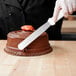 A person using a Tablecraft baking spatula to cut a chocolate cake.