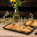 A Clipper Mill black rectangular grid basket filled with pastries on a counter with flowers.
